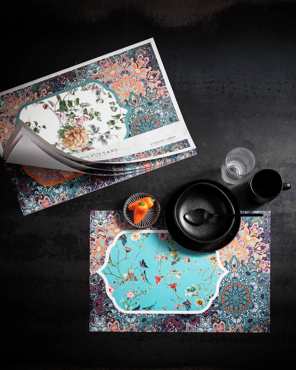 tovagliette in blocco di carta ambientate su tavolo nero, grafica floreale azzura blocchi fiori azzurro bianco